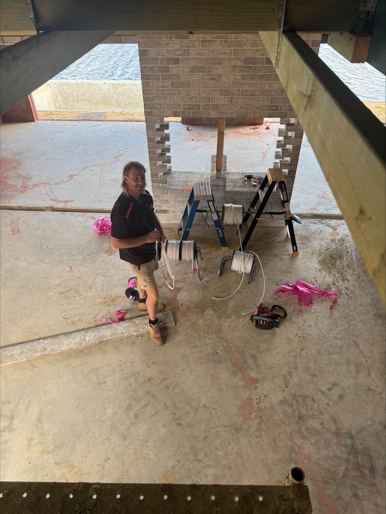 Electrician roughing in cabling at a new canal-front home build in Mandurah with cable reels and ladders on site
